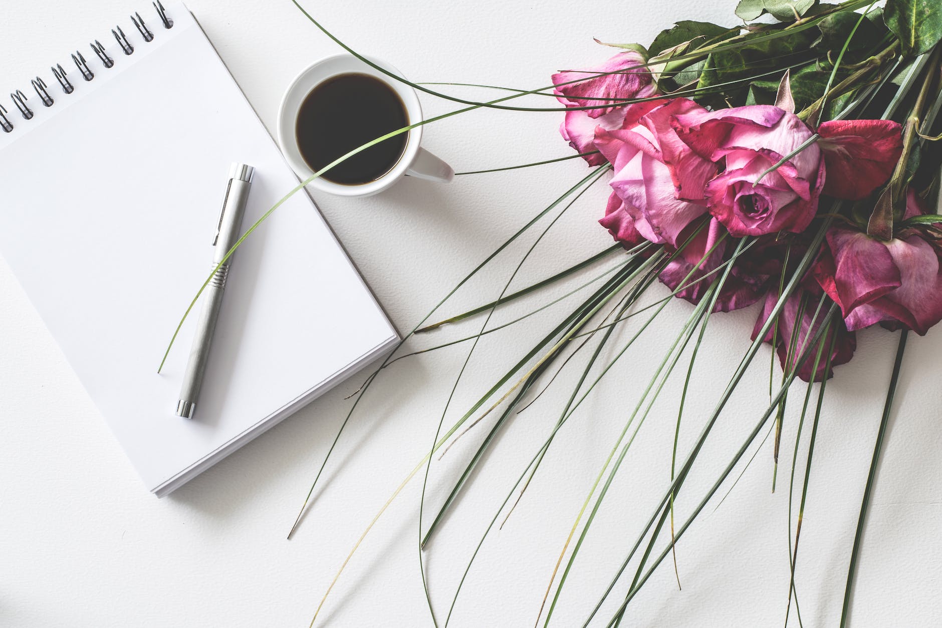 red rose flowers bouquet on white surface beside spring book with click pen and cup of cofffee